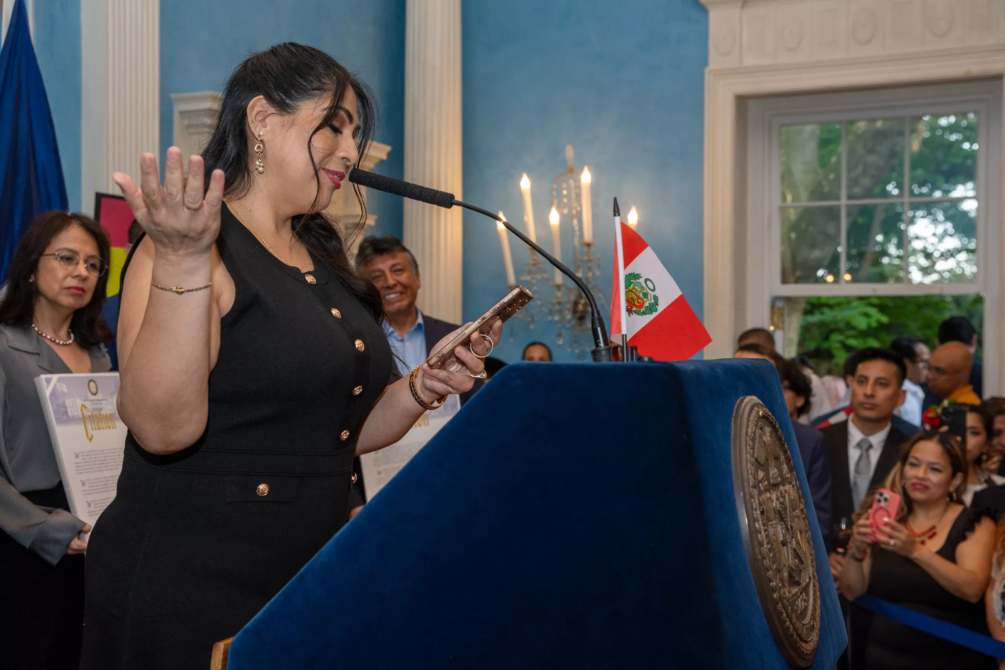 Woman speaking at a podium with a Peruvian flag during a formal recognition event