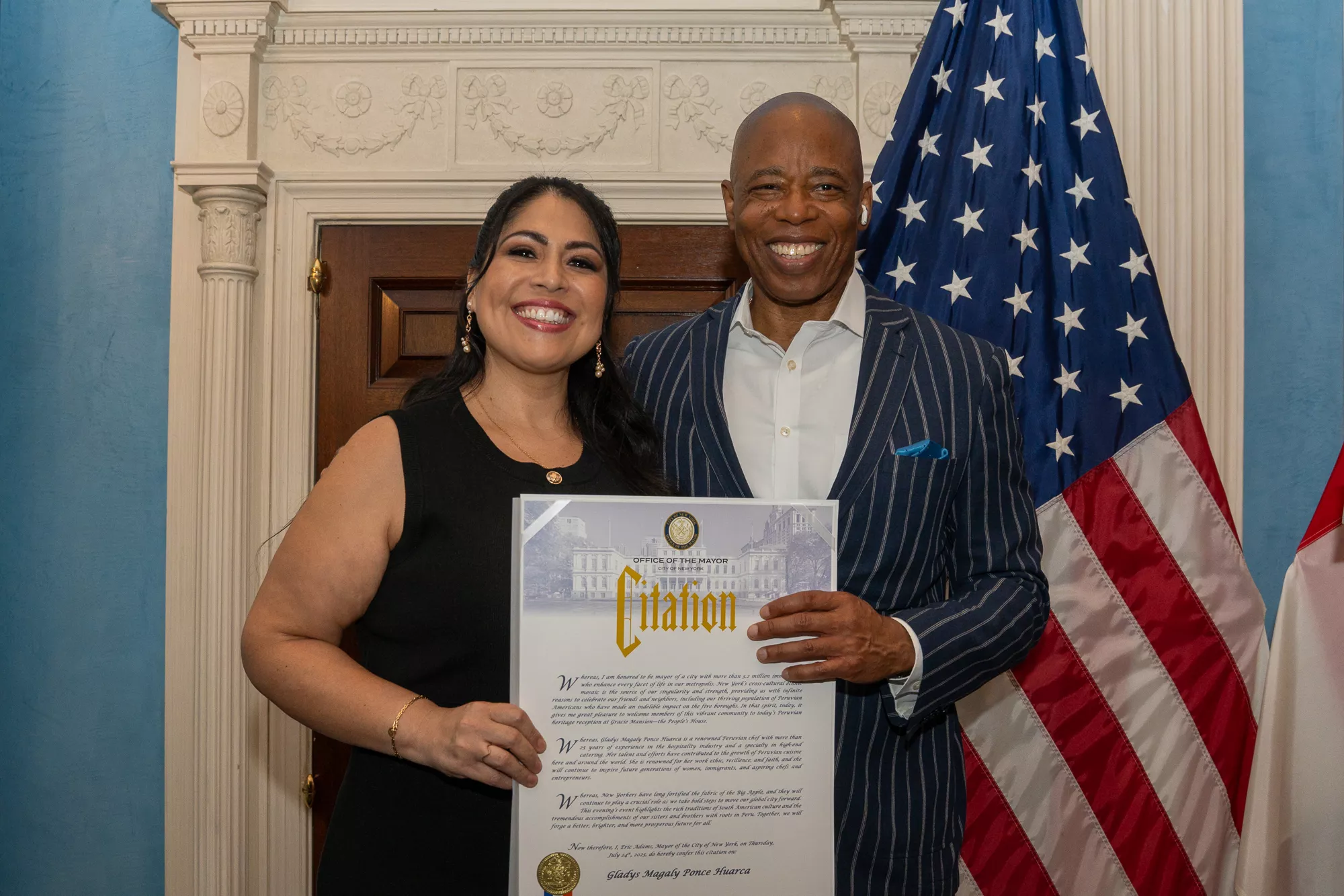 Woman receiving a mayoral citation next to Eric Adams with U.S. and Peruvian flags
